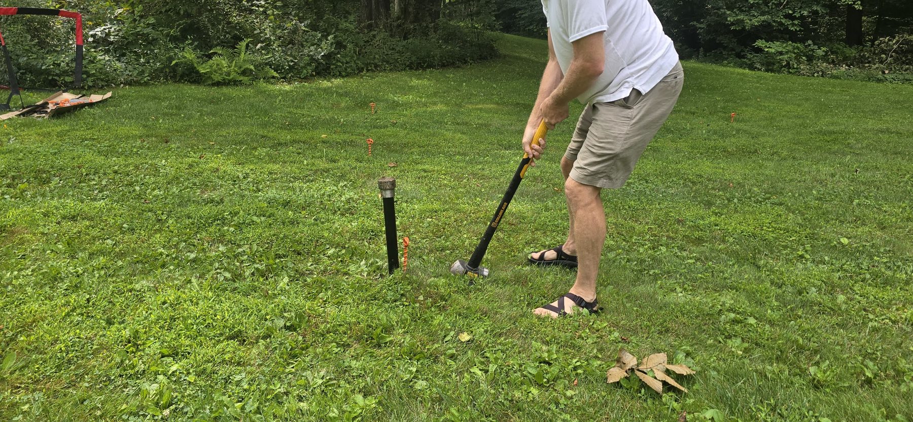 A sledgehammer striking the top of a ground sleeve set into the grass