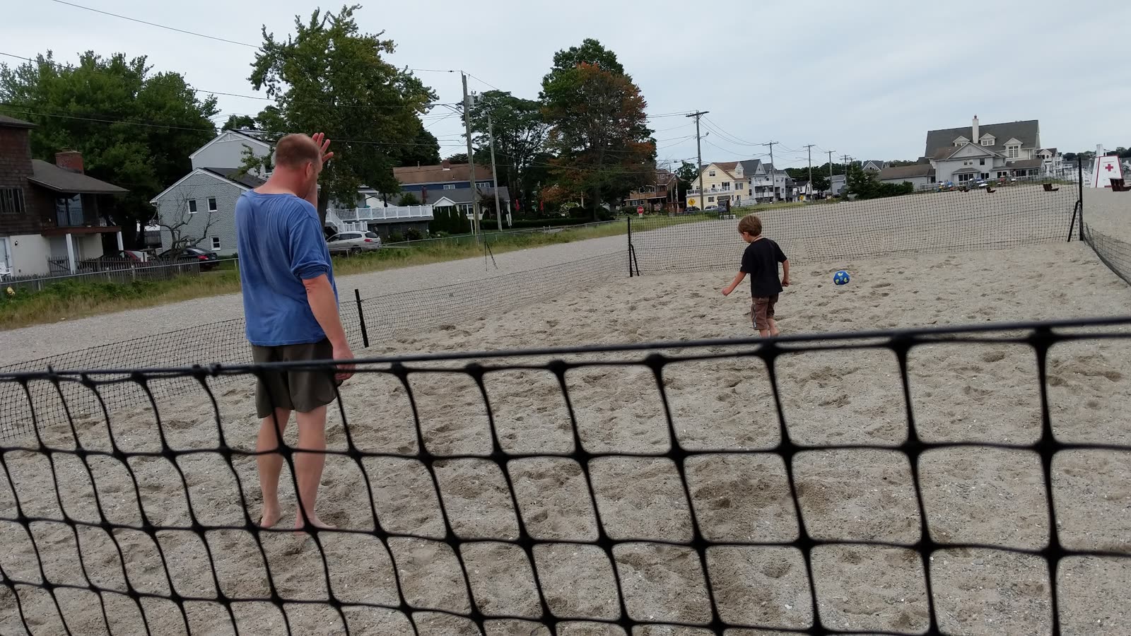 A man and a boy either side of the perimeter netting on the beach