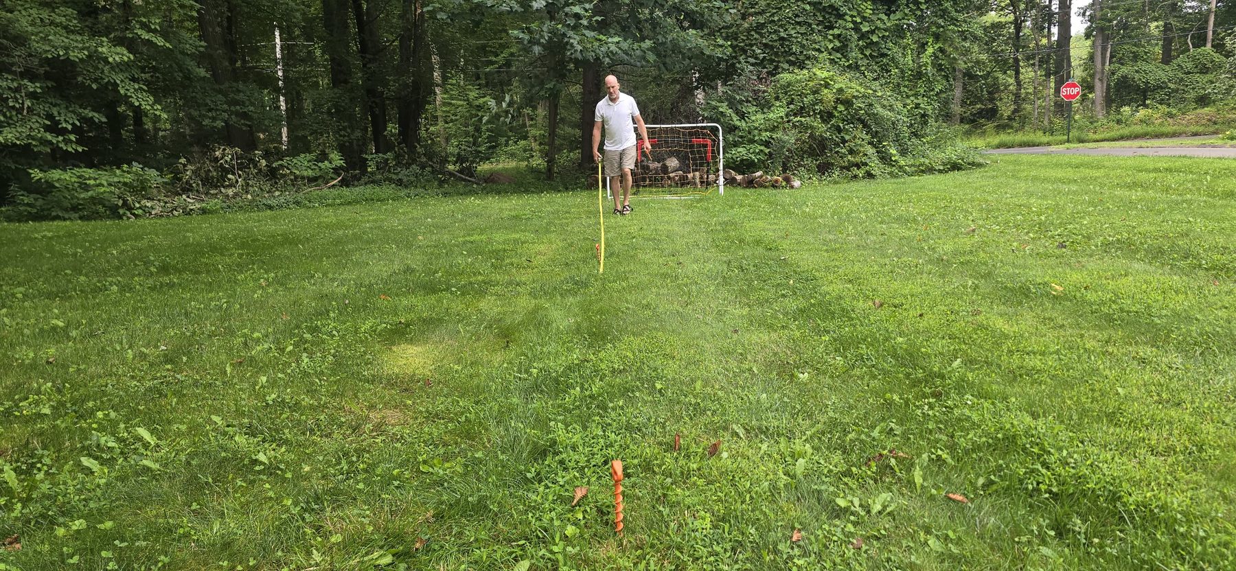 Wide backyard view with a soccer goal at the far end and a person measuring the playing area