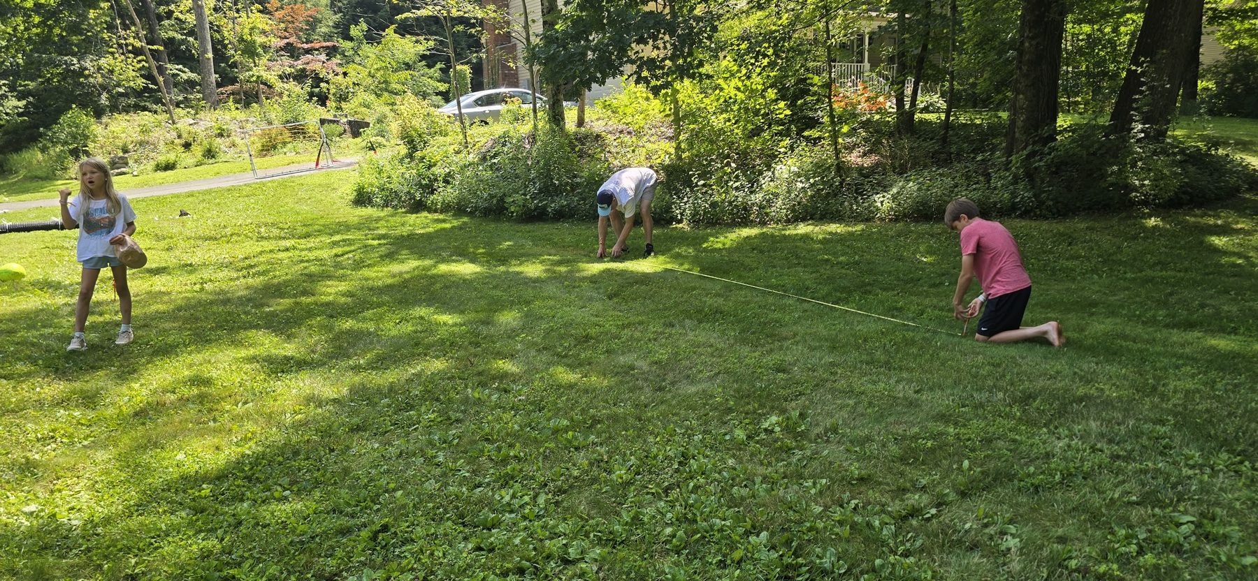 Wide view of a shaded backyard with three people setting out the SoccerYards field across the grass