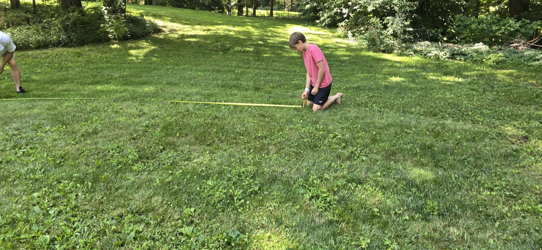 A child walking alongside the yellow measuring tape stretched across the lawn