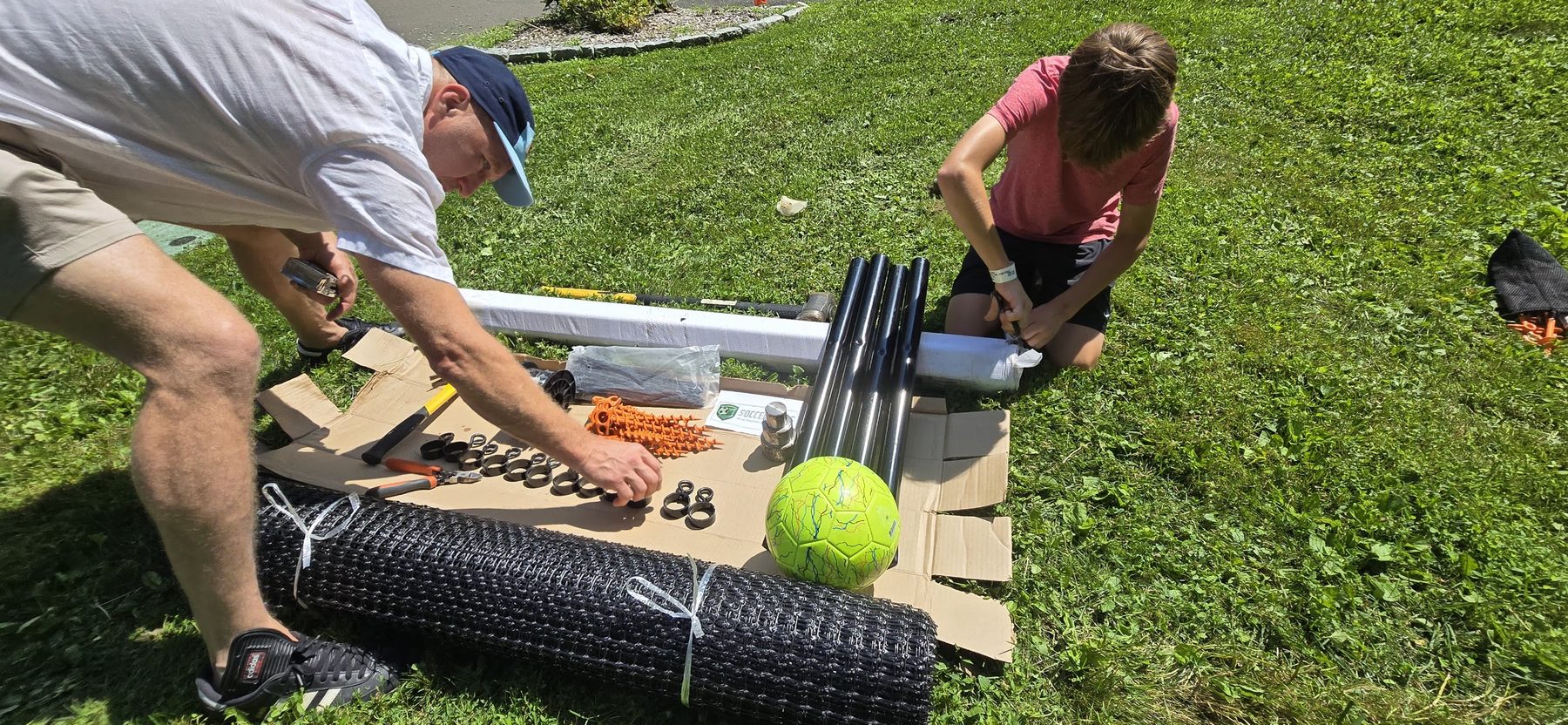 An adult and a child unrolling the SoccerYards wall panel across the lawn