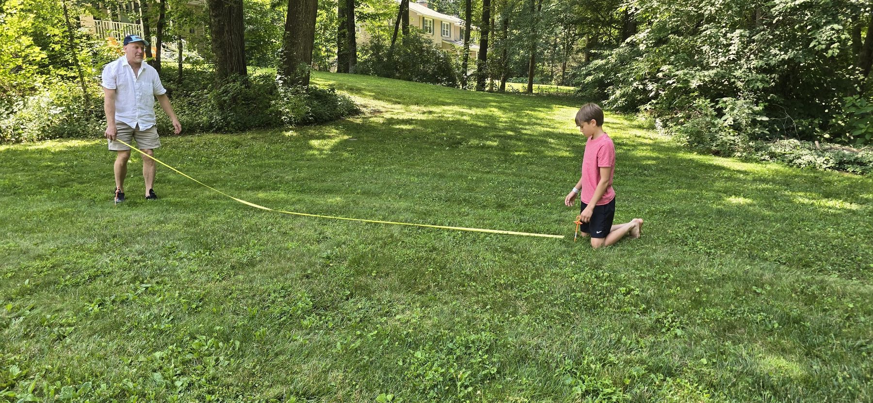 Two people walking a yellow tape line across a backyard to set out the field perimeter